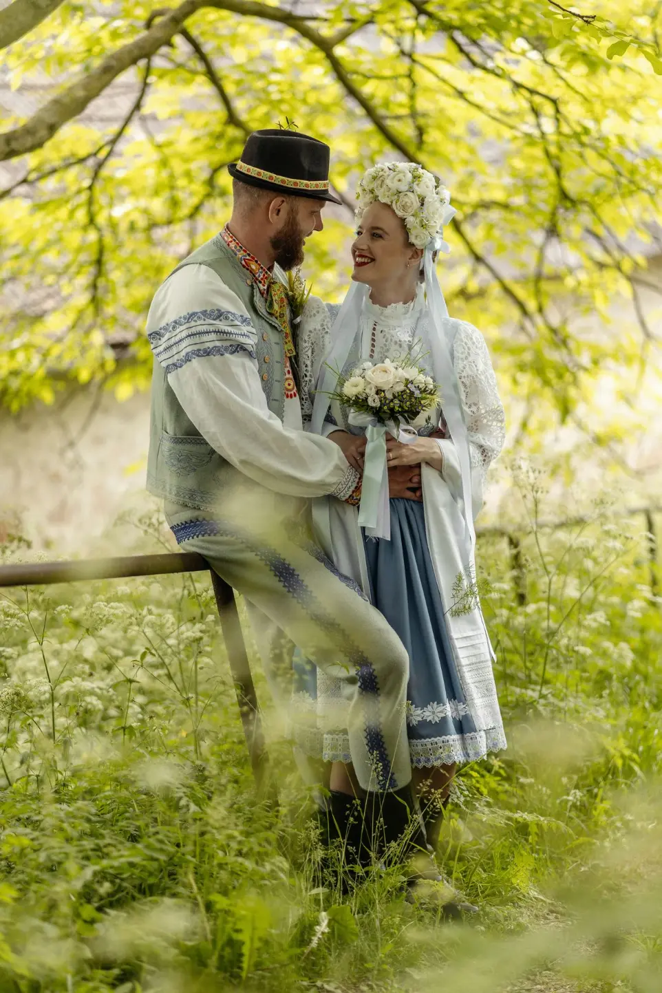 A bride and groom lovingly hold each other’s hands, standing face to face with soft smiles. The bride’s white gown flows gently in the breeze, and the groom wears a tailored suit.