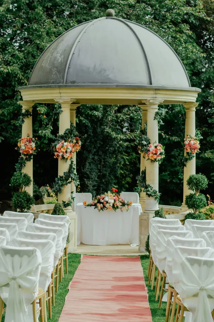 .Bride and Groom at Elegant Wedding Venue The bride and groom stand together at the center of a beautifully decorated wedding venue. Surrounded by elegant floral arrangements, soft draping, and warm fairy lights, the couple shares a quiet, intimate moment. The venue features a romantic arch and perfectly arranged seating, creating a magical atmosphere for their special day.